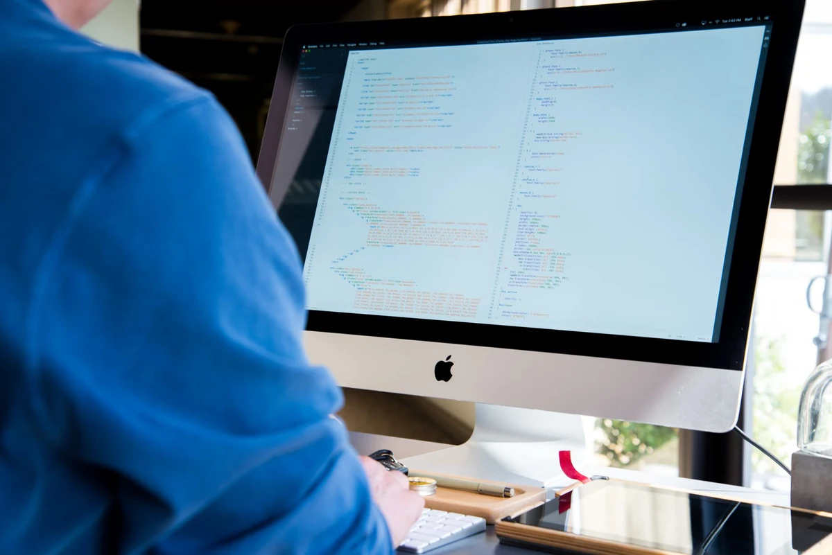 Un programmatore con una camicia blu che codifica su un iMac. Perfetto per temi tecnologici o legati al lavoro.